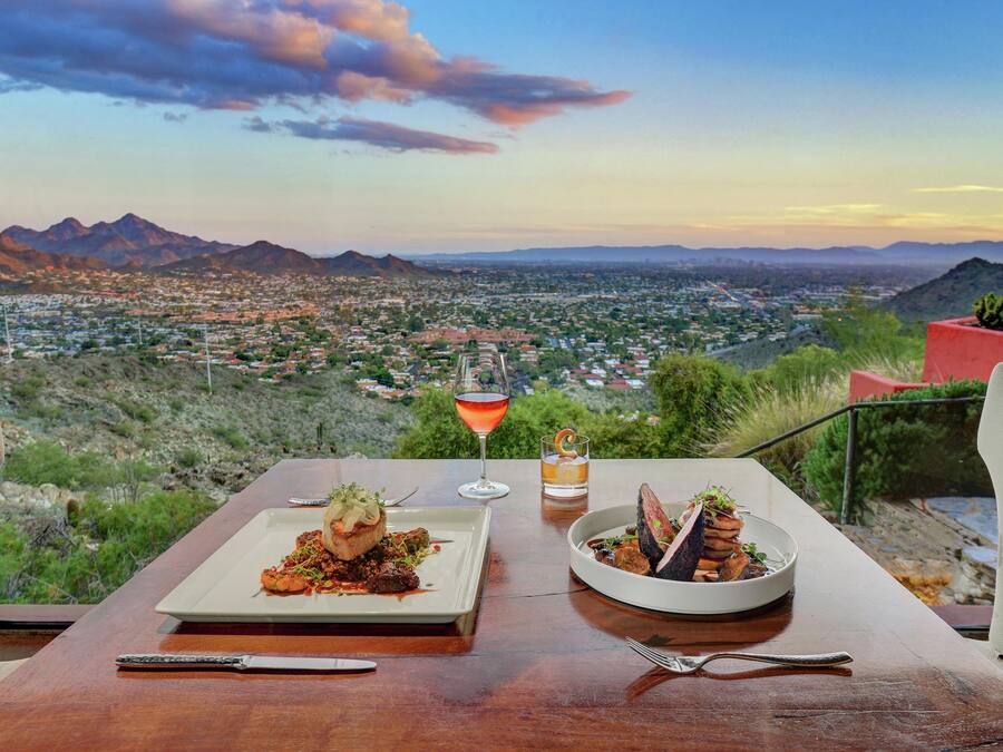 Una mesa con dos platos y una bebida, con vistas a un paisaje urbano y montañas.