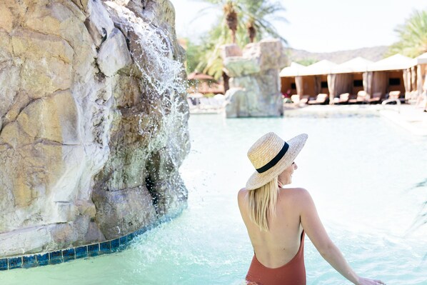 A woman in a swimsuit and straw hat by a pool with a rock waterfall and lounge chairs in the background. - Hilton Phoenix Tapatio Cliffs Resort (Phoenix)