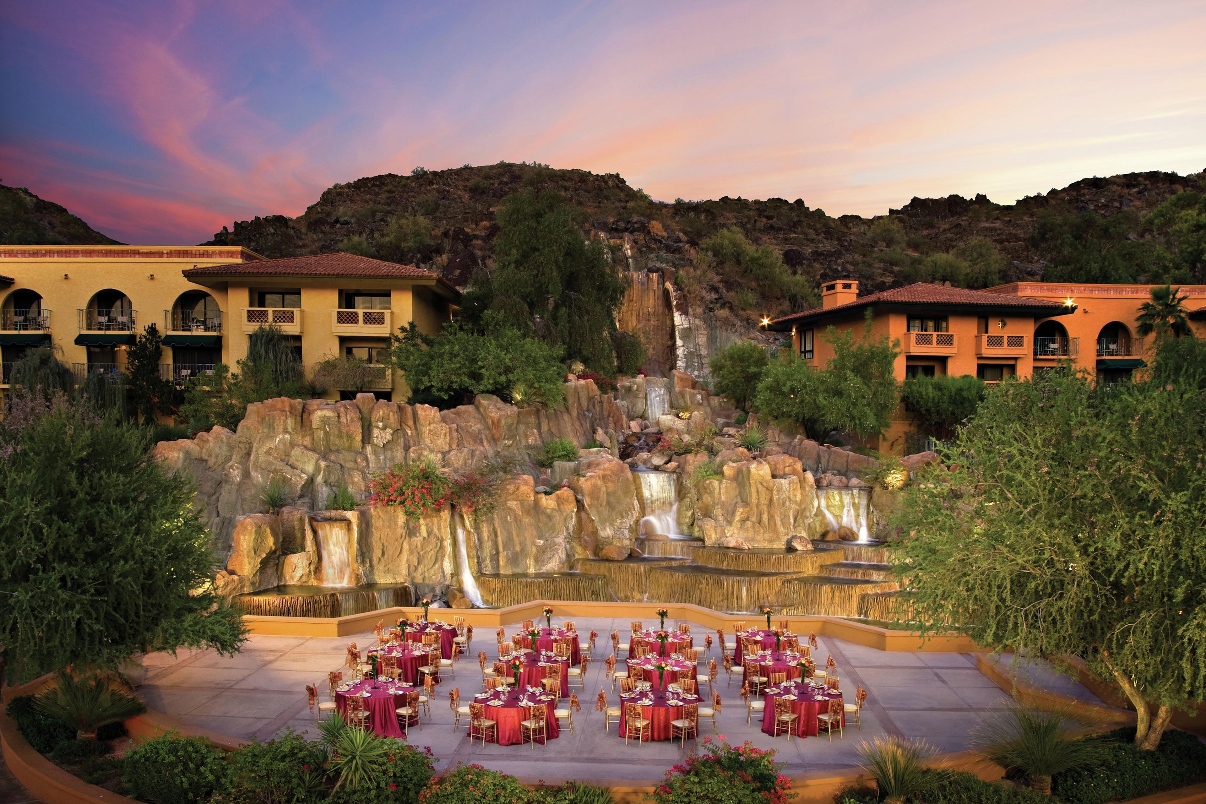 A resort with outdoor dining, a waterfall, and buildings with balconies.