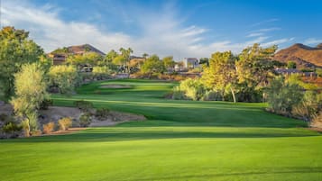 A golf course with a clear sky, surrounded by trees and hills.