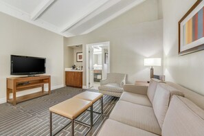 A living room with a TV, sofa, bench, patterned carpet, and a door leading to a bathroom.