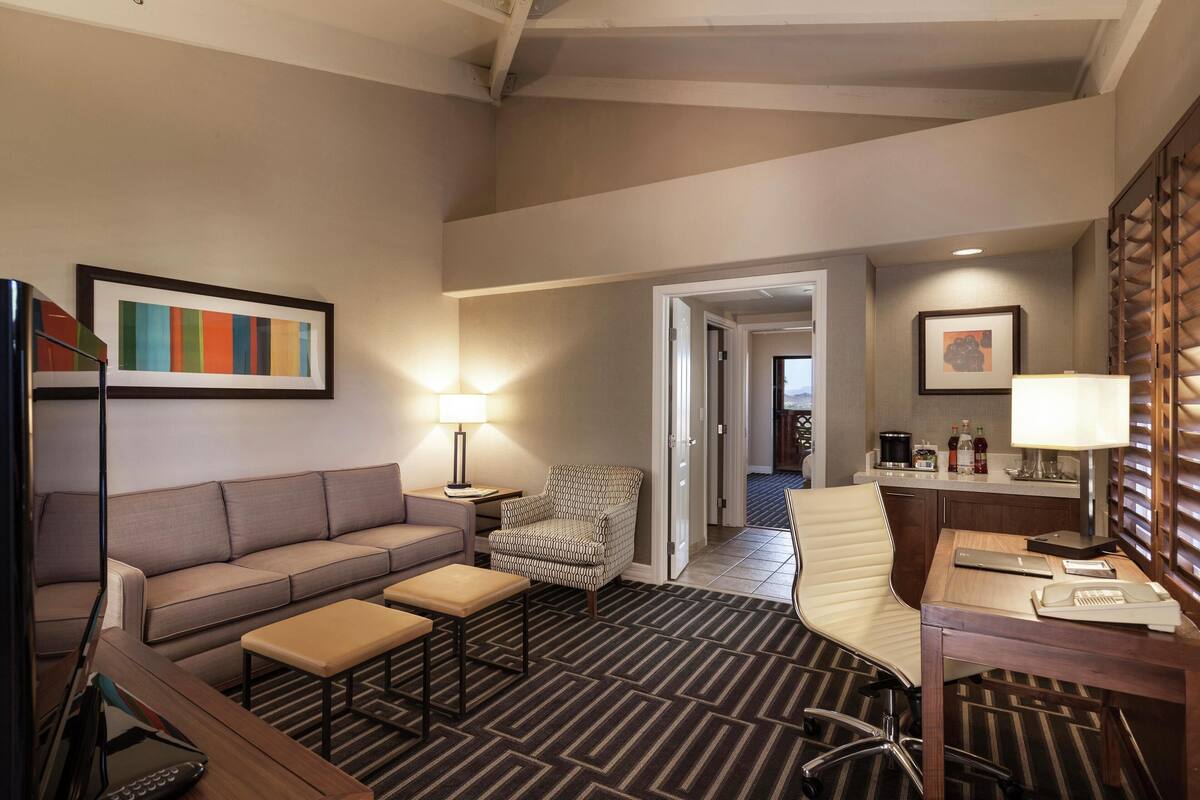 Habitación de hotel con sofá, sillón, escritorio y alfombra a rayas.
