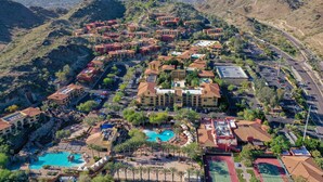 An aerial view of a resort with multiple buildings, a swimming pool, and a mountainous backdrop.