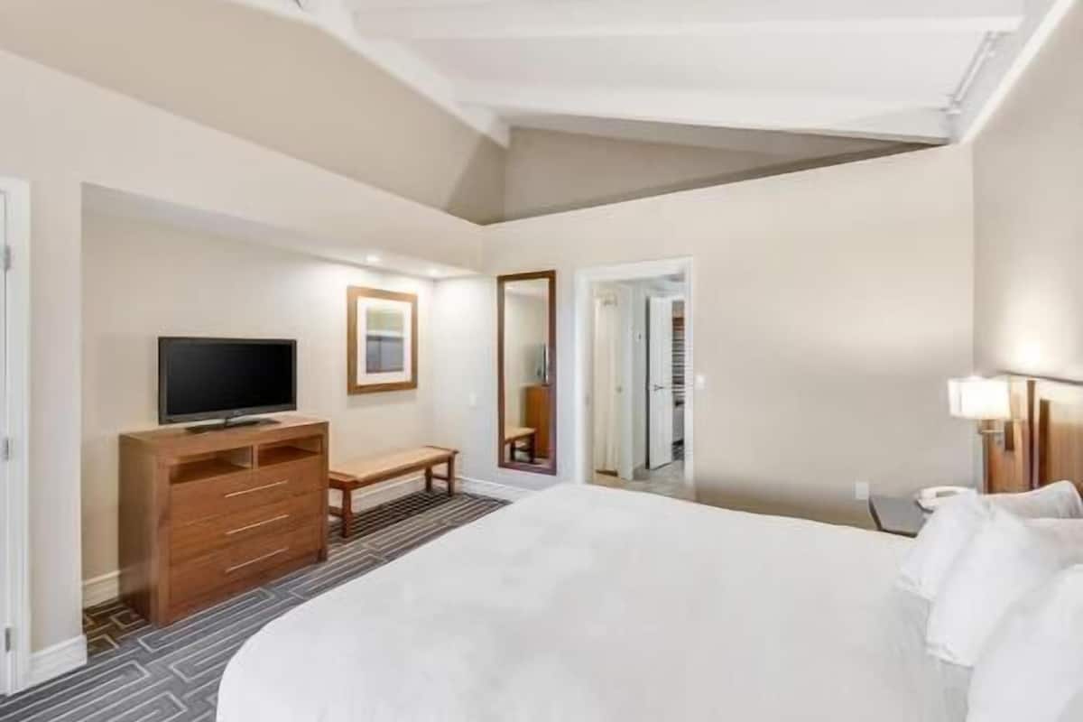 A hotel room with a large bed, a TV, a wooden dresser, a bench, and a mirror.