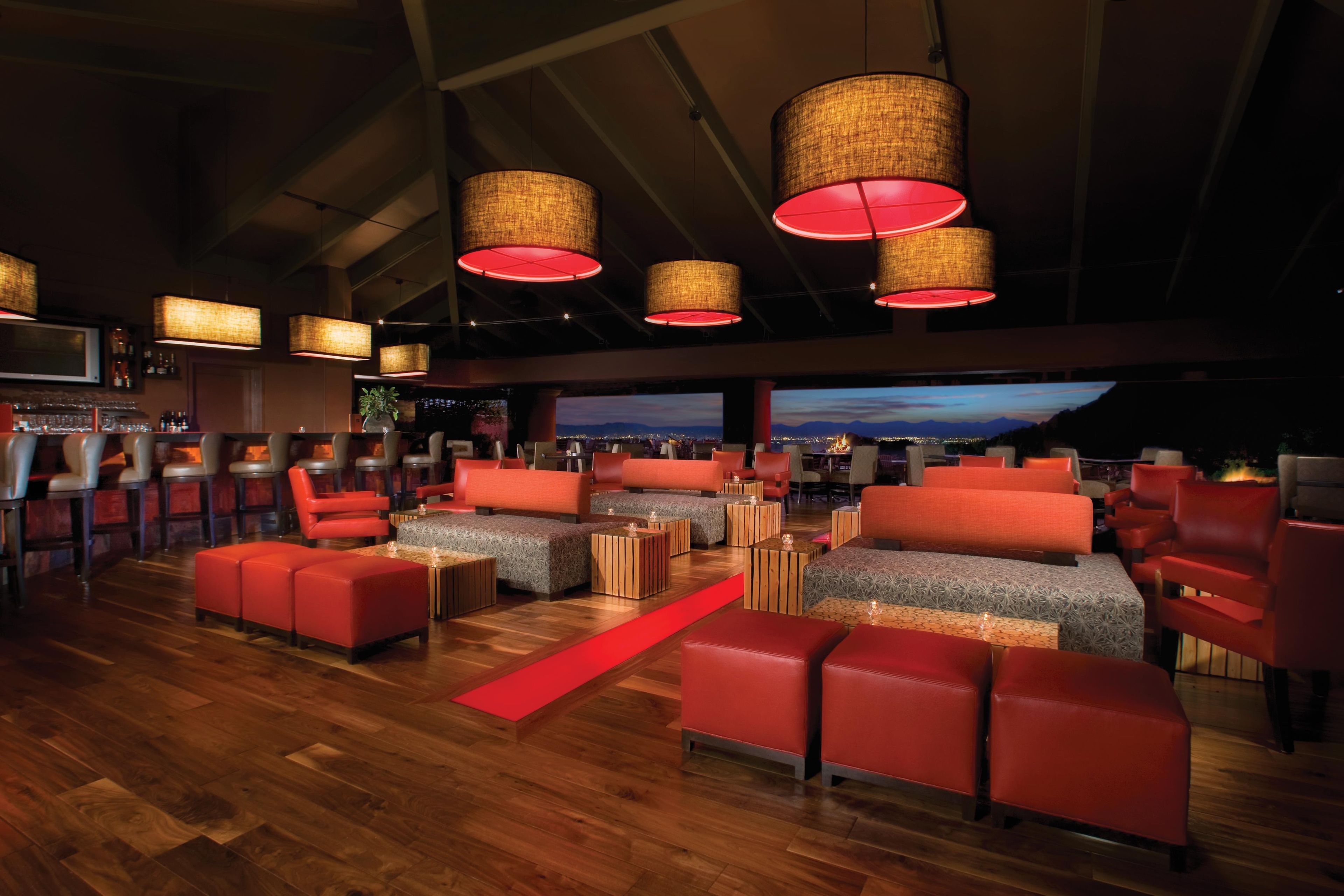 A bar area with red upholstered seating, wooden tables, and hanging wicker lamps.