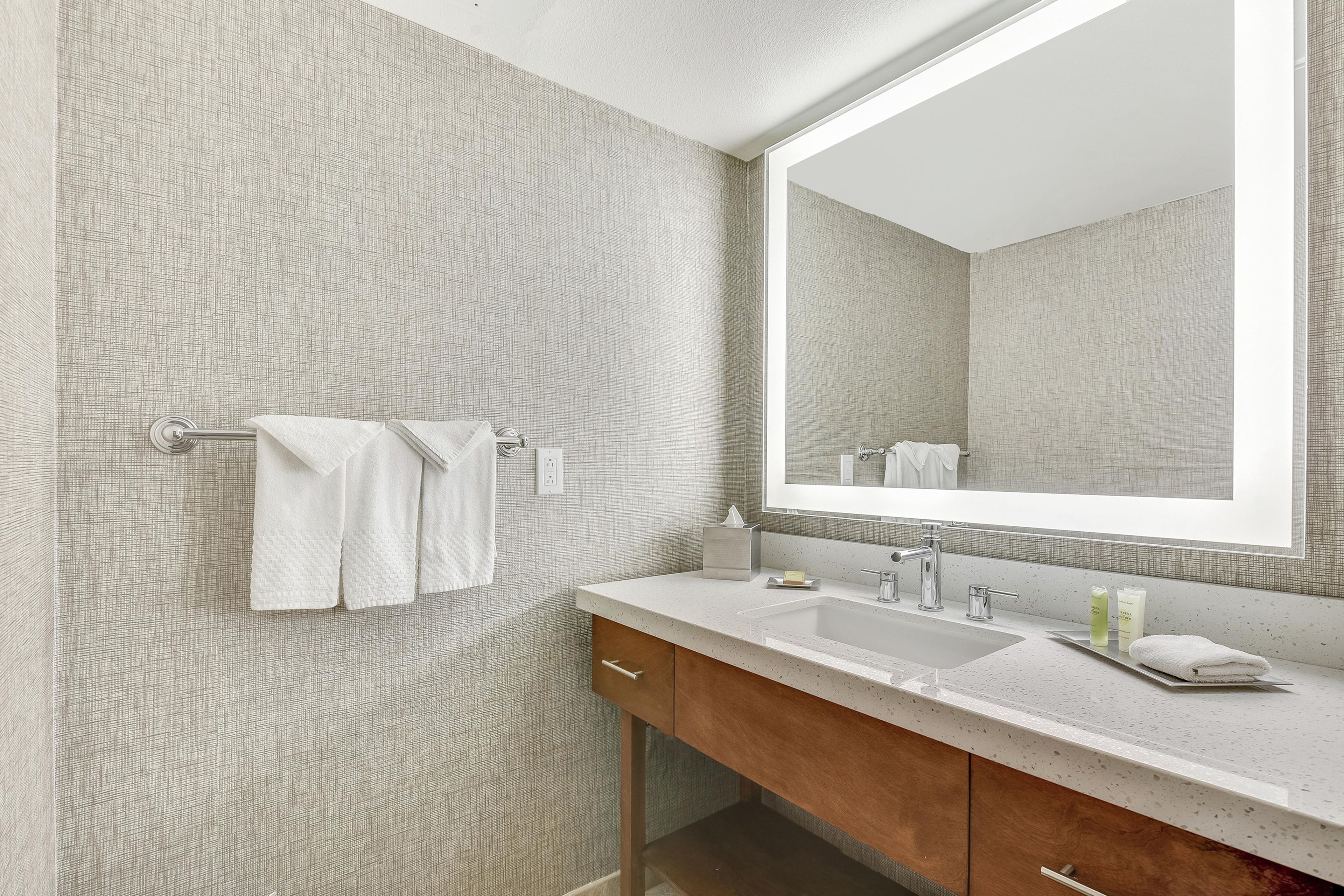 A bathroom with a large mirror, a sink, and a towel rack.