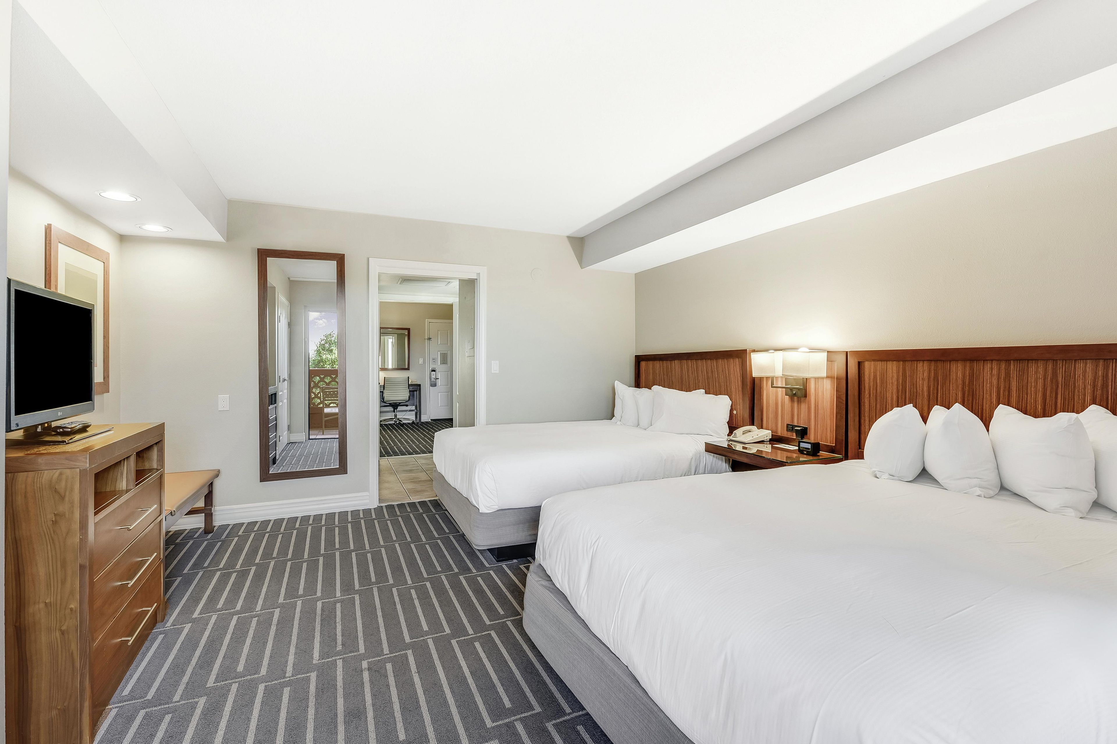 A hotel room with two beds, a TV, a wooden dresser, and a mirror.