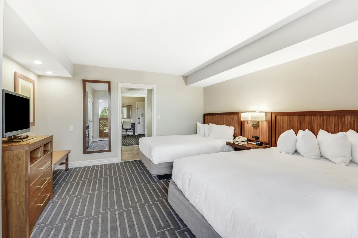 A hotel room with two beds, a TV, a wooden dresser, and a mirror.