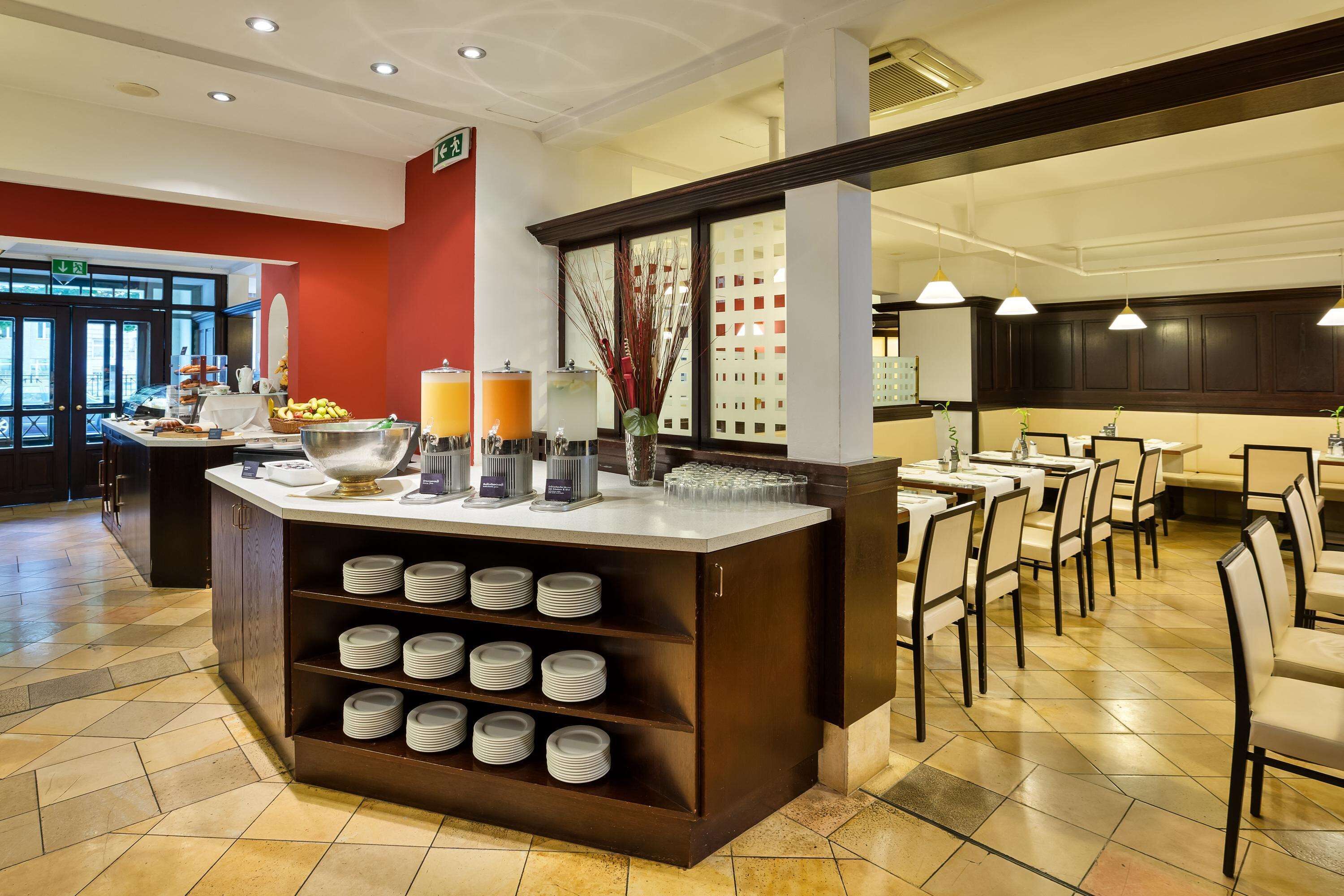 Eine Hotelhalle mit einer Rezeption, einem Buffetbereich und einer Sitzecke mit Tischen und Stühlen.