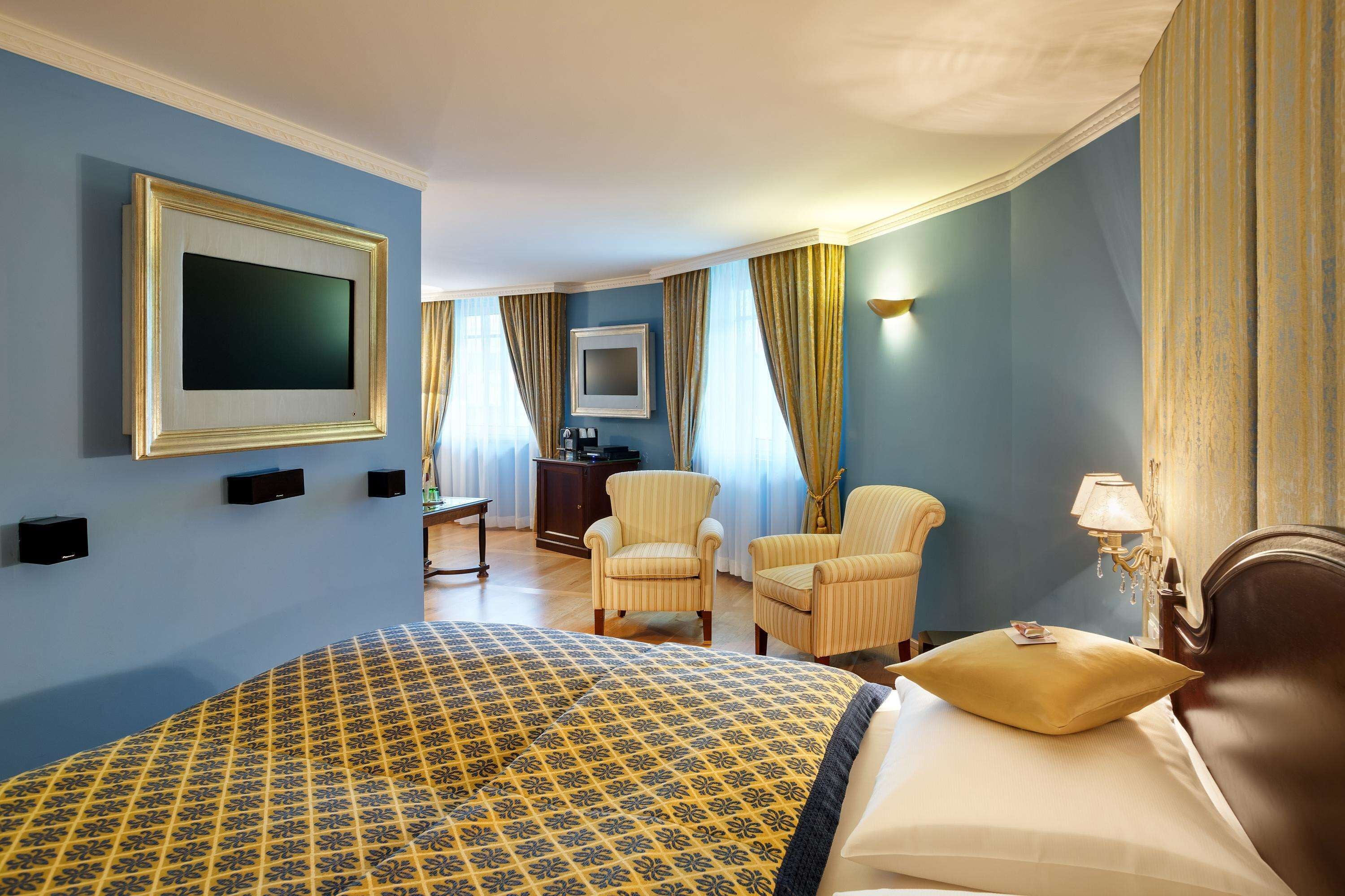 Una habitación de hotel con una cama grande, dos sillones, un televisor y un escritorio con una lámpara.