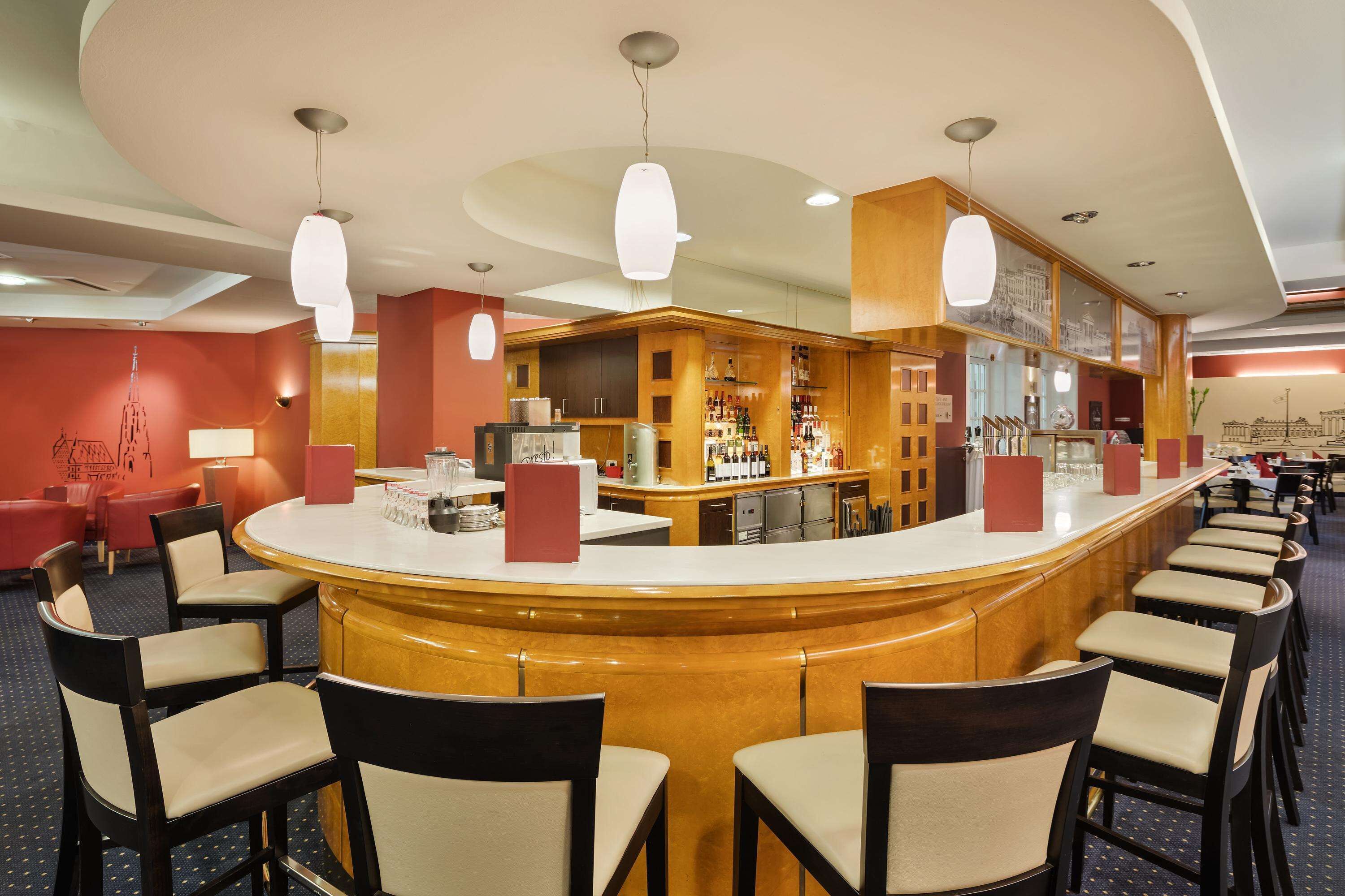 A bar area with a curved counter, multiple seating options, and a variety of bottles and glasses on shelves.