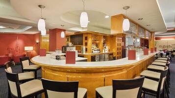 A bar area with a curved counter, multiple seating options, and a variety of bottles and glasses on shelves.