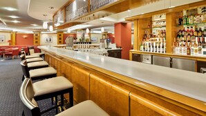 Zona de bar con una barra alargada, varios taburetes y una variedad de botellas de licores.