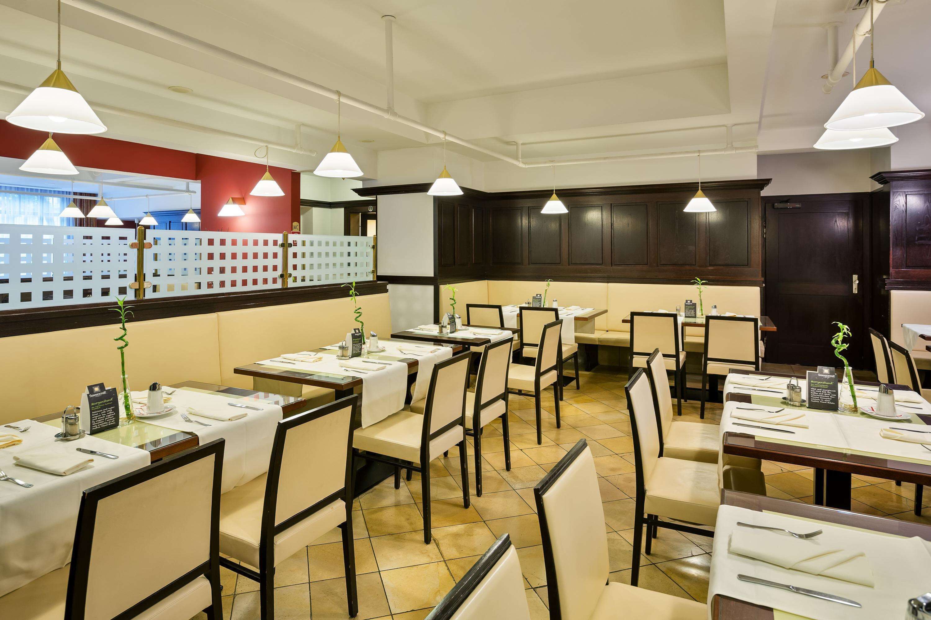 Un restaurante con varias mesas y sillas, manteles blancos e iluminación colgante.
