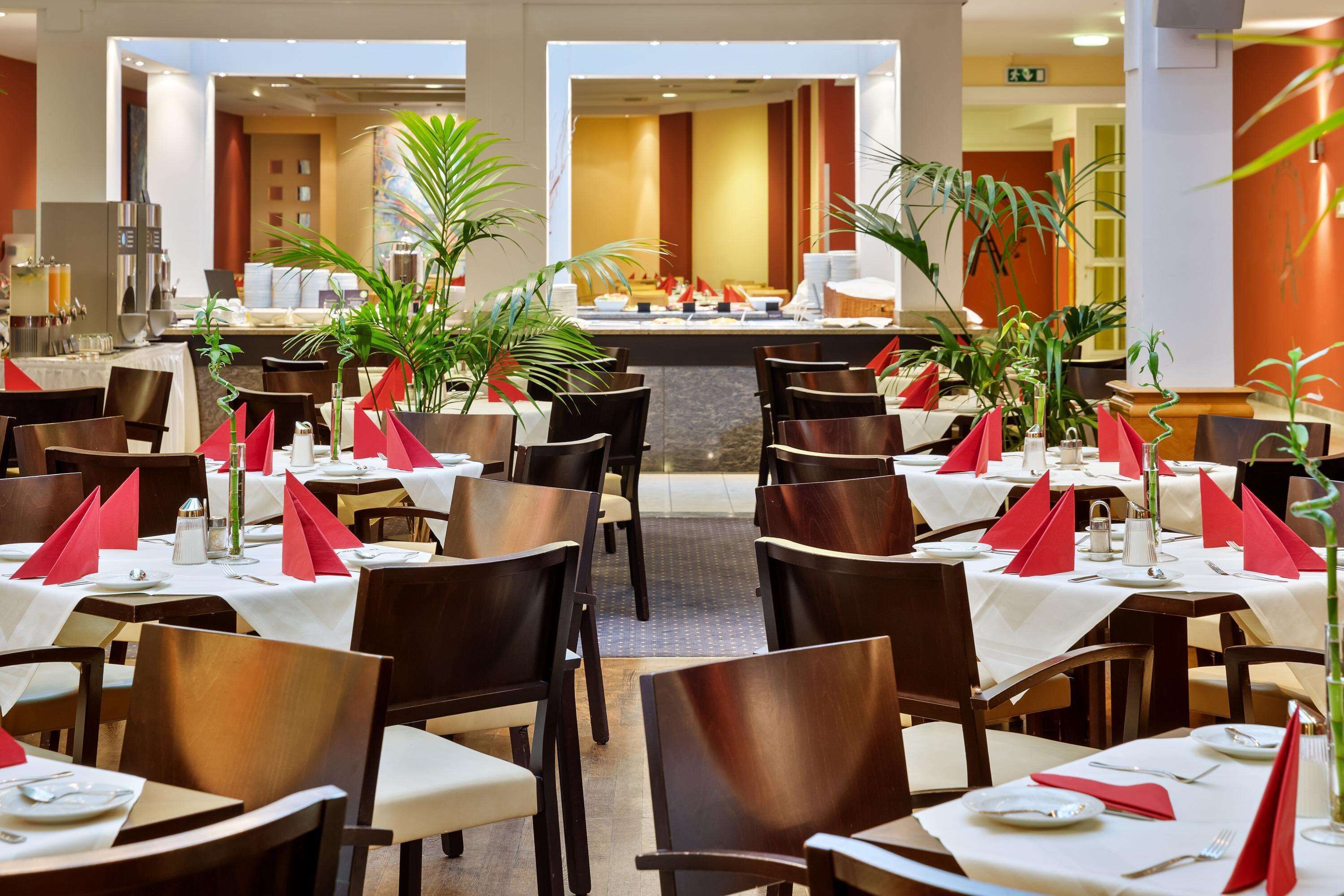 A restaurant with multiple tables, each set with red napkins, white tablecloths, and dark wooden chairs.