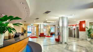 Un moderno vestíbulo de hotel con una recepción, asientos rojos y una planta grande.