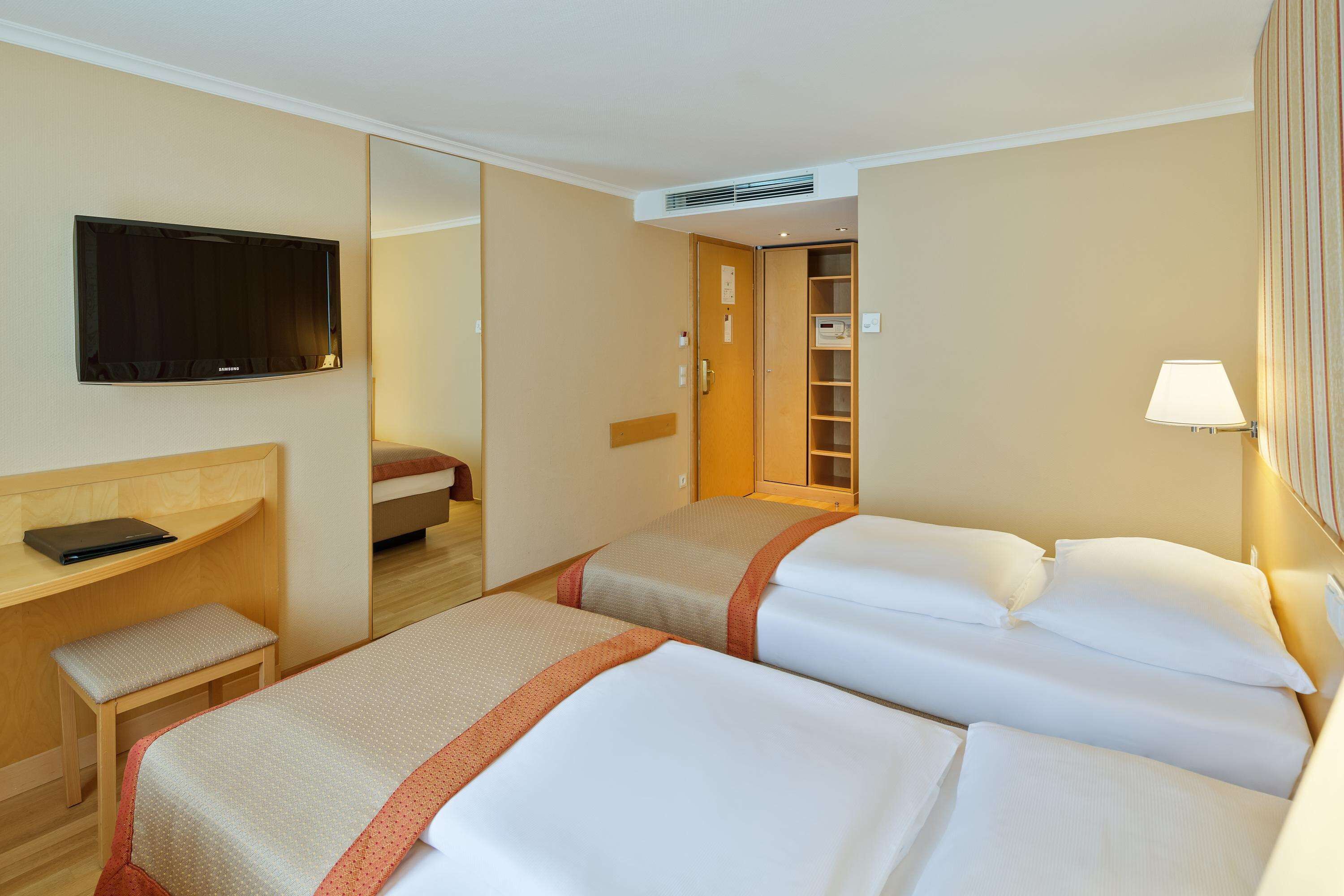Una habitación de hotel con dos camas, un escritorio, una silla, un televisor y una lámpara.
