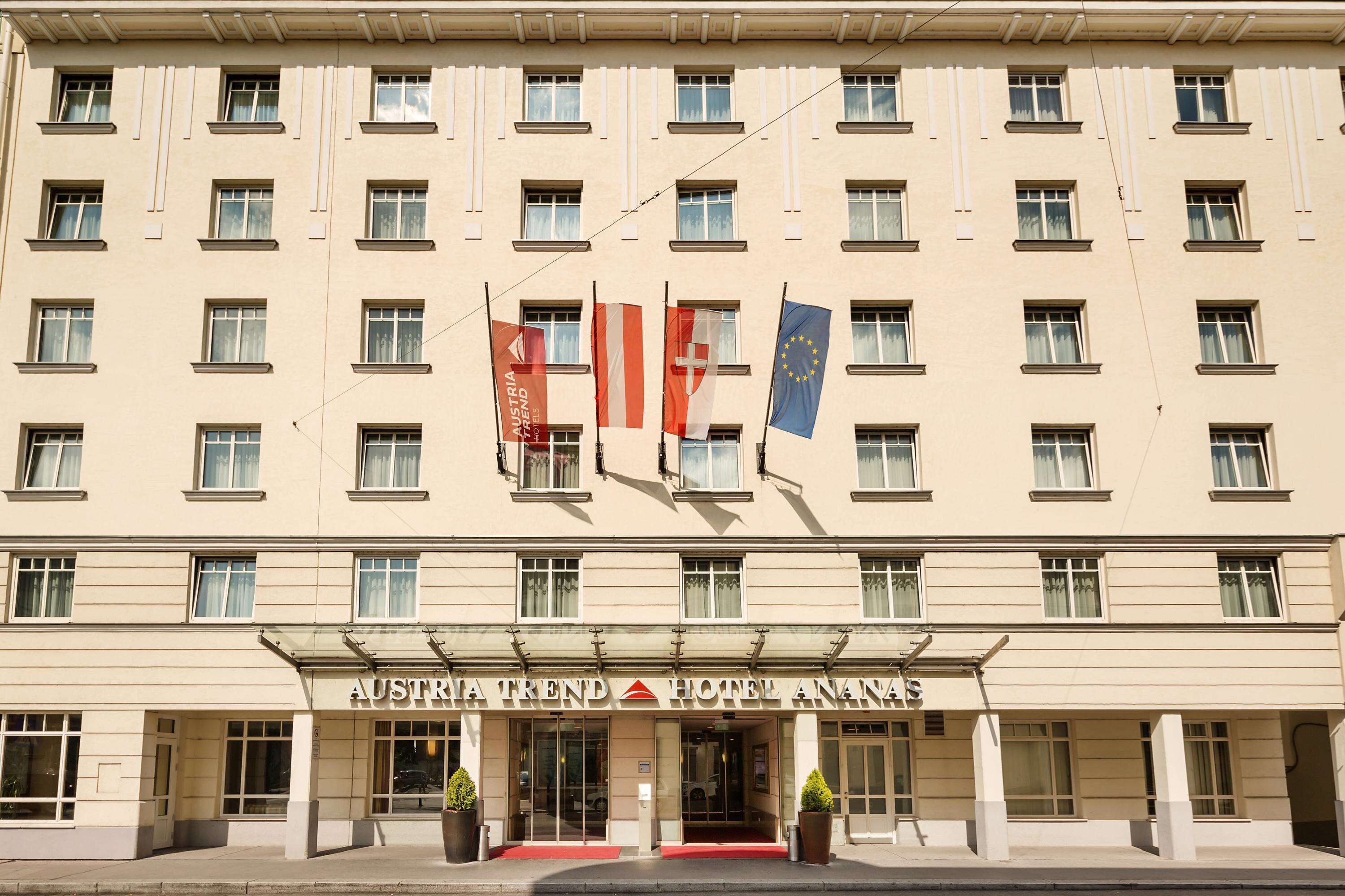 Fachada de hotel com várias janelas, bandeiras e uma entrada imponente com tapete vermelho.