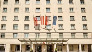 Fachada de hotel com várias janelas, bandeiras e uma entrada imponente com tapete vermelho.
