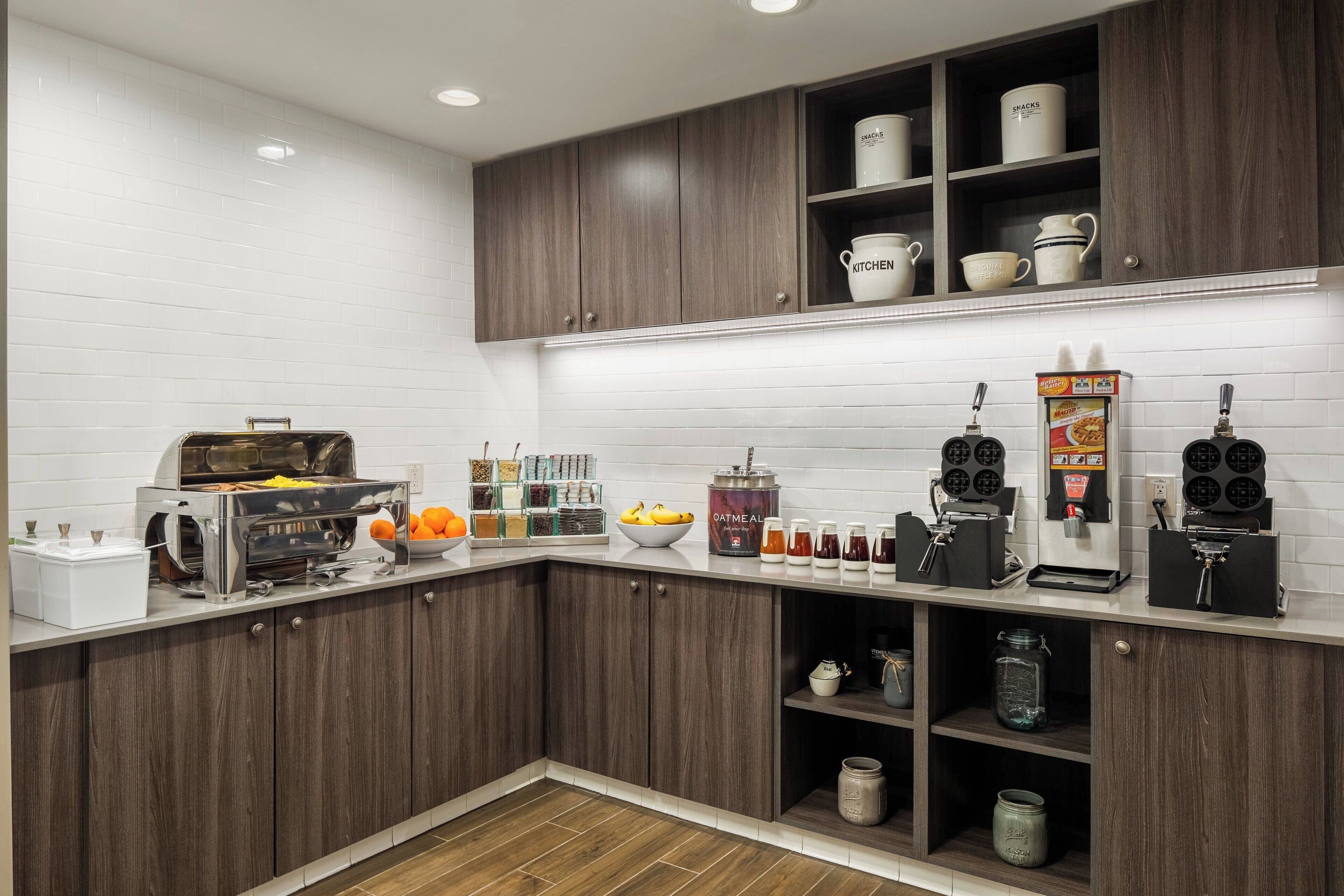 A modern kitchen with dark wood cabinets, white subway tiles, and various appliances including a coffee machine and waffle maker.