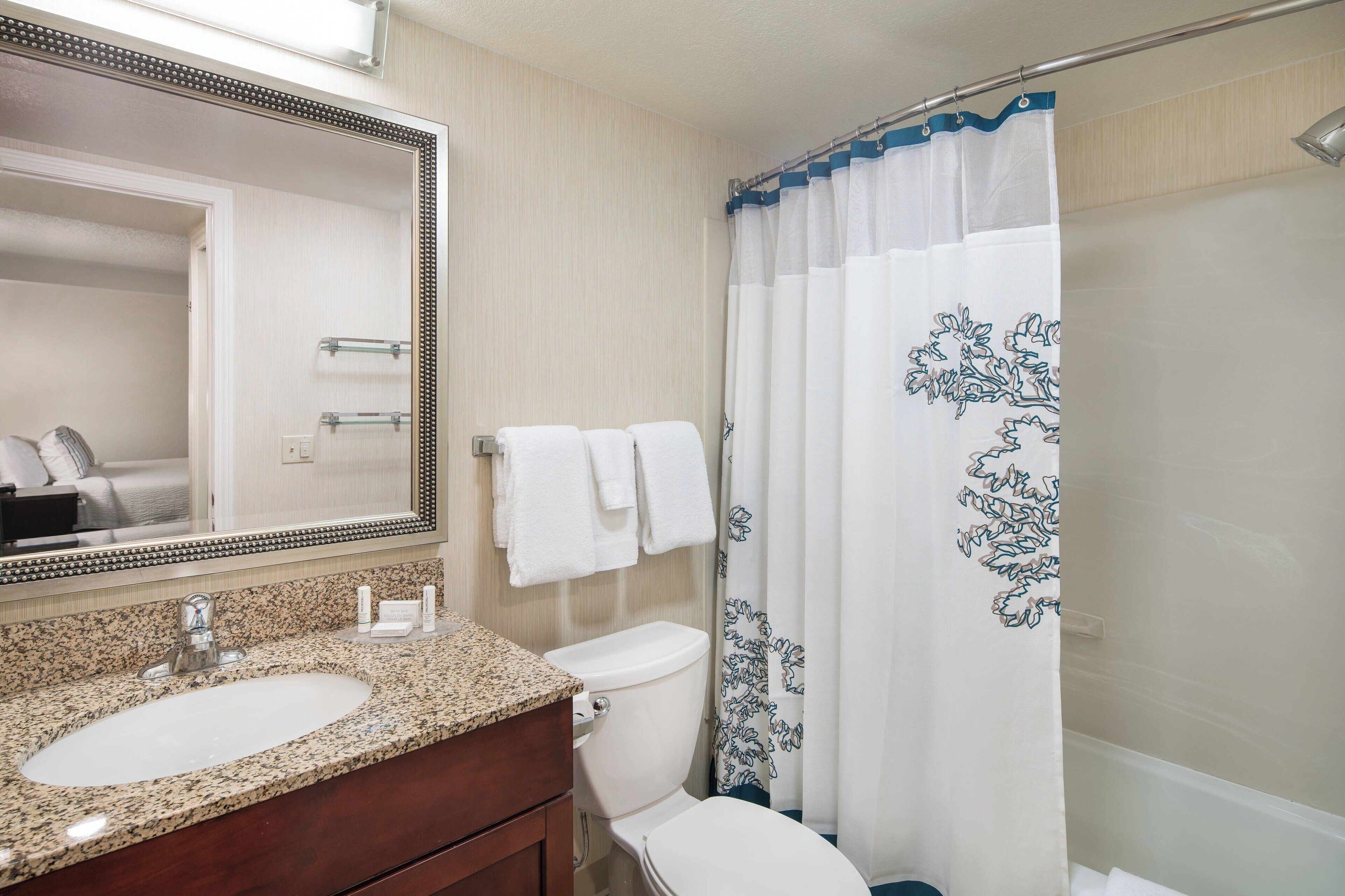 A bathroom with a granite countertop sink, a white toilet, and a shower curtain with a floral pattern.