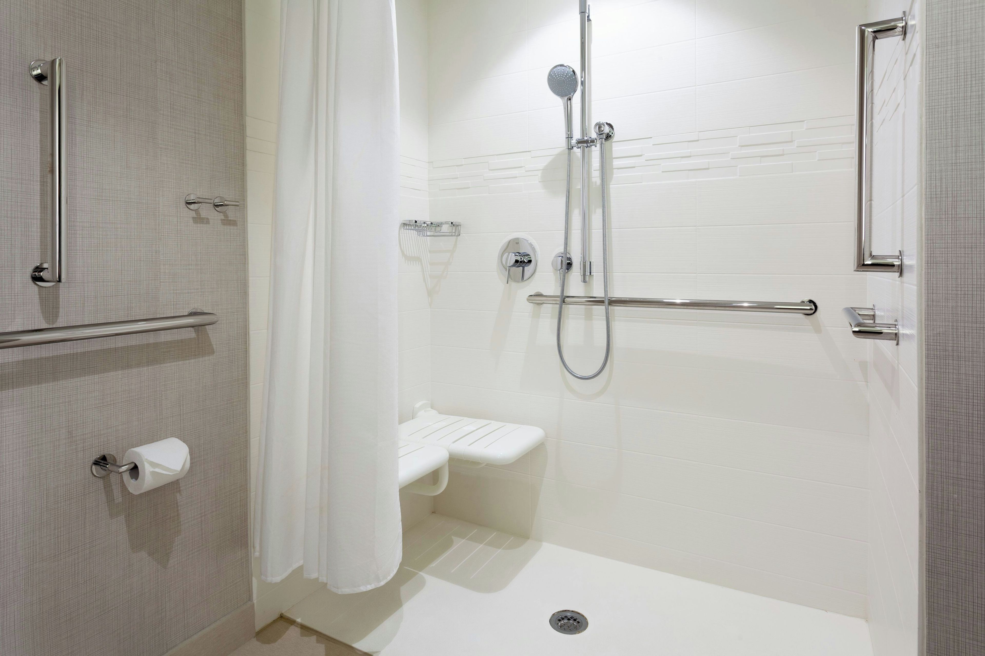 A modern bathroom with a shower, toilet, and handrail.