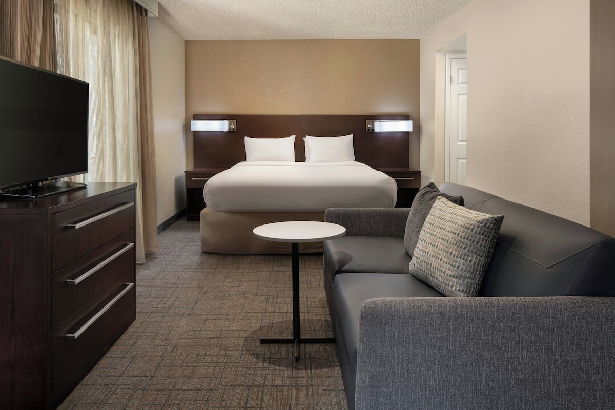 A hotel room with a bed, a TV on a dresser, a small round table, a sofa, and a nightstand.