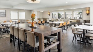 A spacious hotel dining area with multiple tables and chairs, a central wooden table with a vase of flowers, and large windows providing natural light. - Residence Inn by Marriott Pasadena Arcadia (Arcadia)