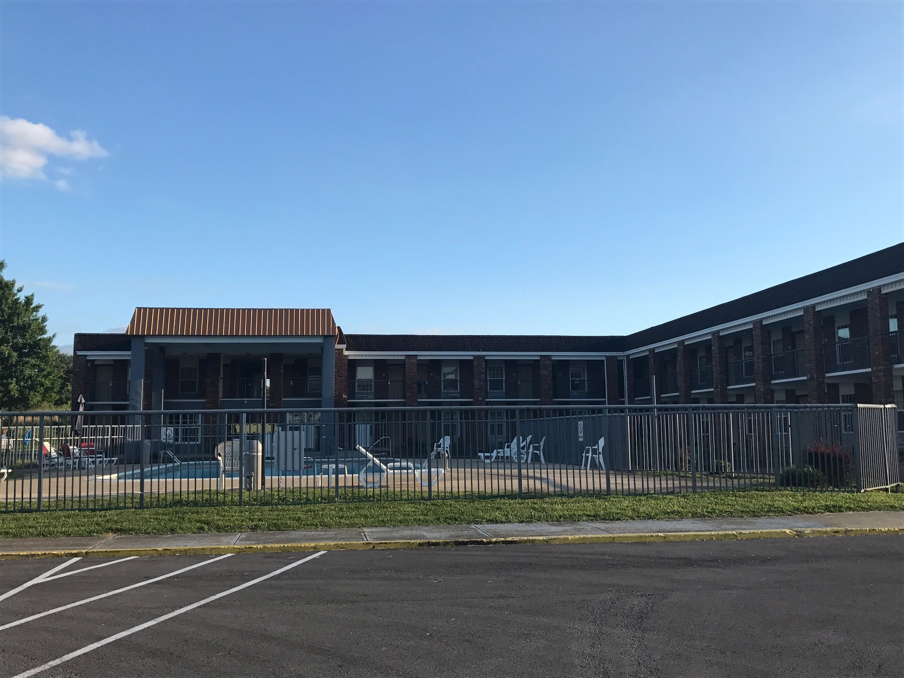 A multi-story building with a flat roof, a covered outdoor area, and a fenced parking lot.