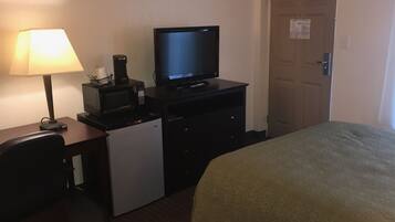 A hotel room with a bed, a desk with a lamp, a microwave, and a television.
