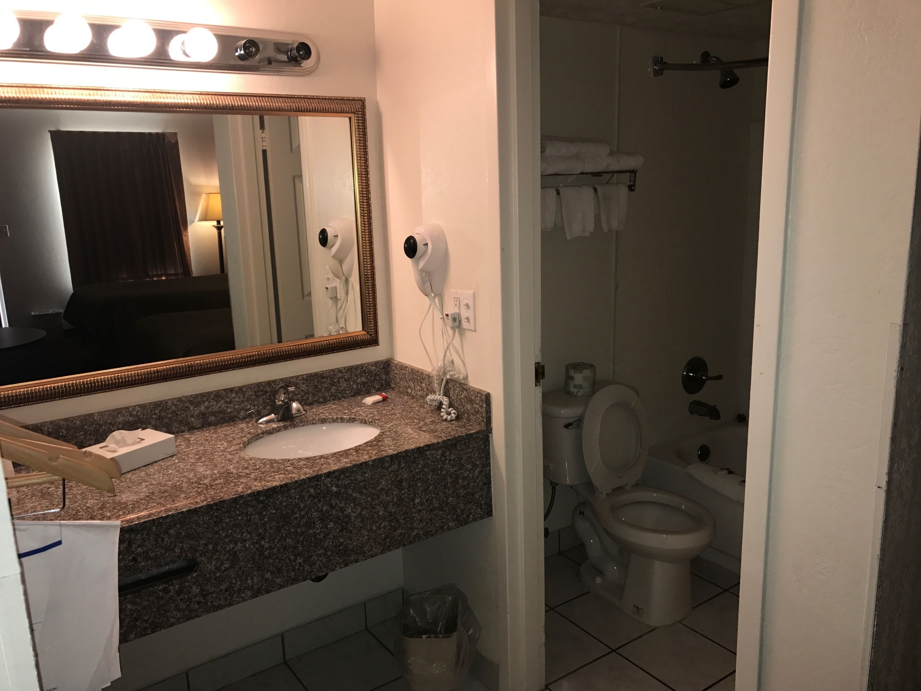 A bathroom with a granite countertop, a sink, a mirror, a hairdryer, and a toilet.