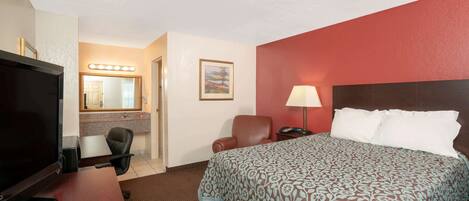 A hotel room with a bed, a desk with a TV, a chair, a lamp, and a painting on the wall.