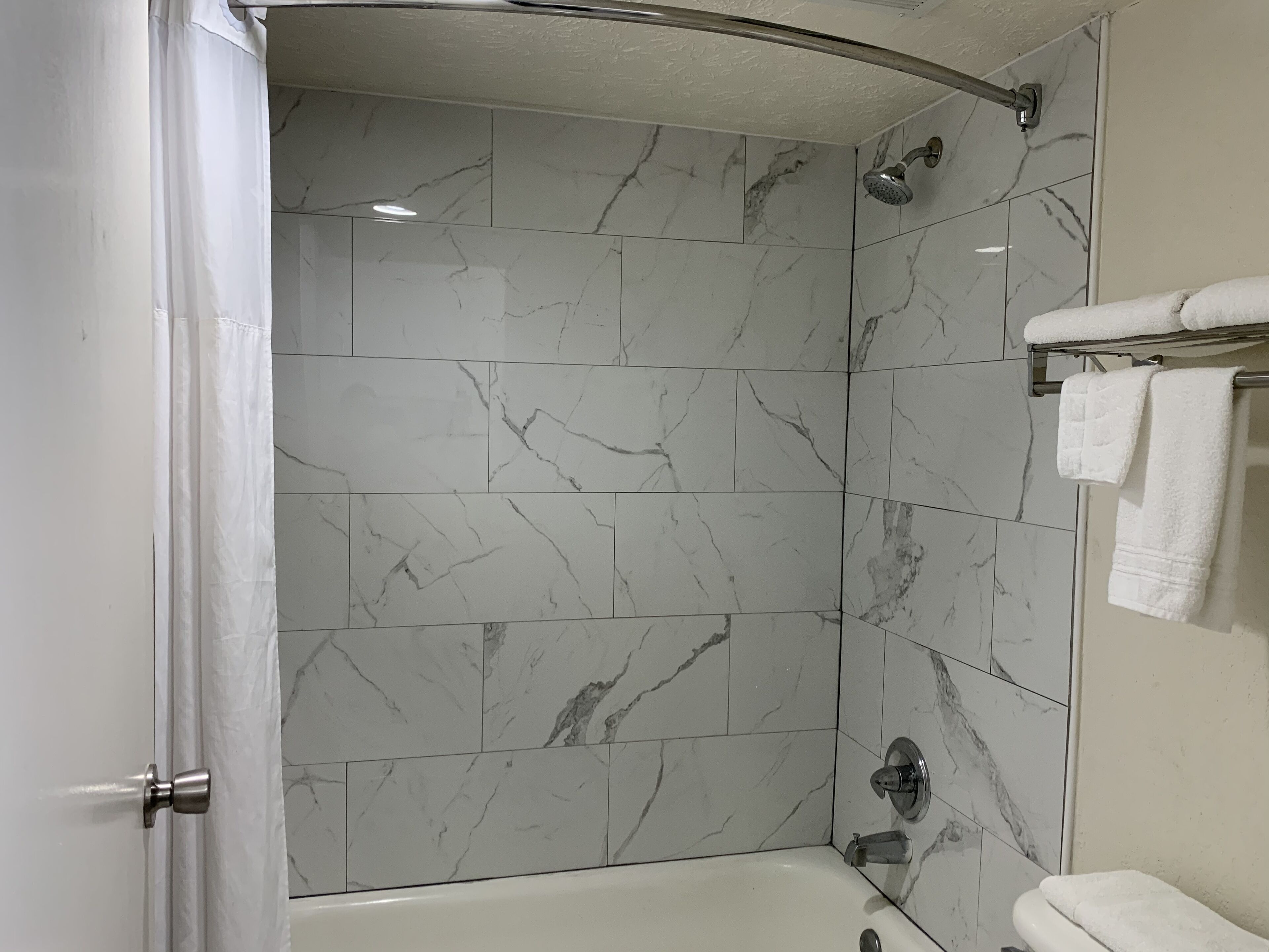 A modern bathroom with a curved shower, marble tiles, a bathtub, and a towel rack.