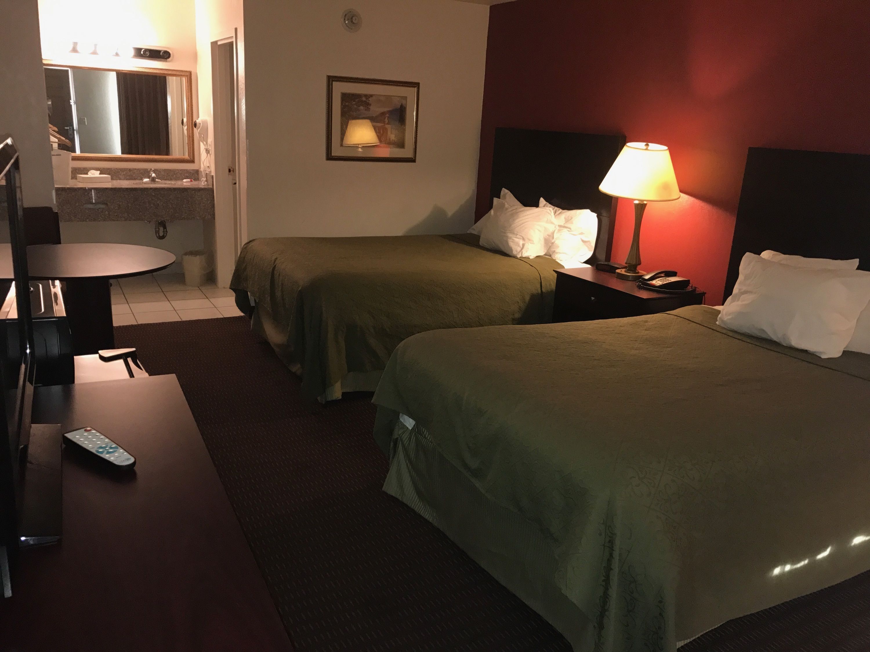 Une chambre d’hôtel avec deux lits, un bureau, une chaise, une lampe et un tableau au mur.