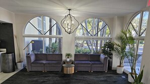 Una sala moderna con dos sofás grises, un tapete negro y una pequeña mesa redonda. Se ven grandes ventanales con vistas a árboles y edificios.