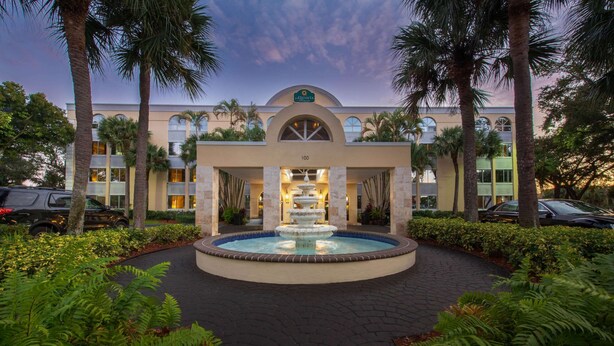 Entrada de hotel con una fuente, palmeras y un camino pavimentado.
