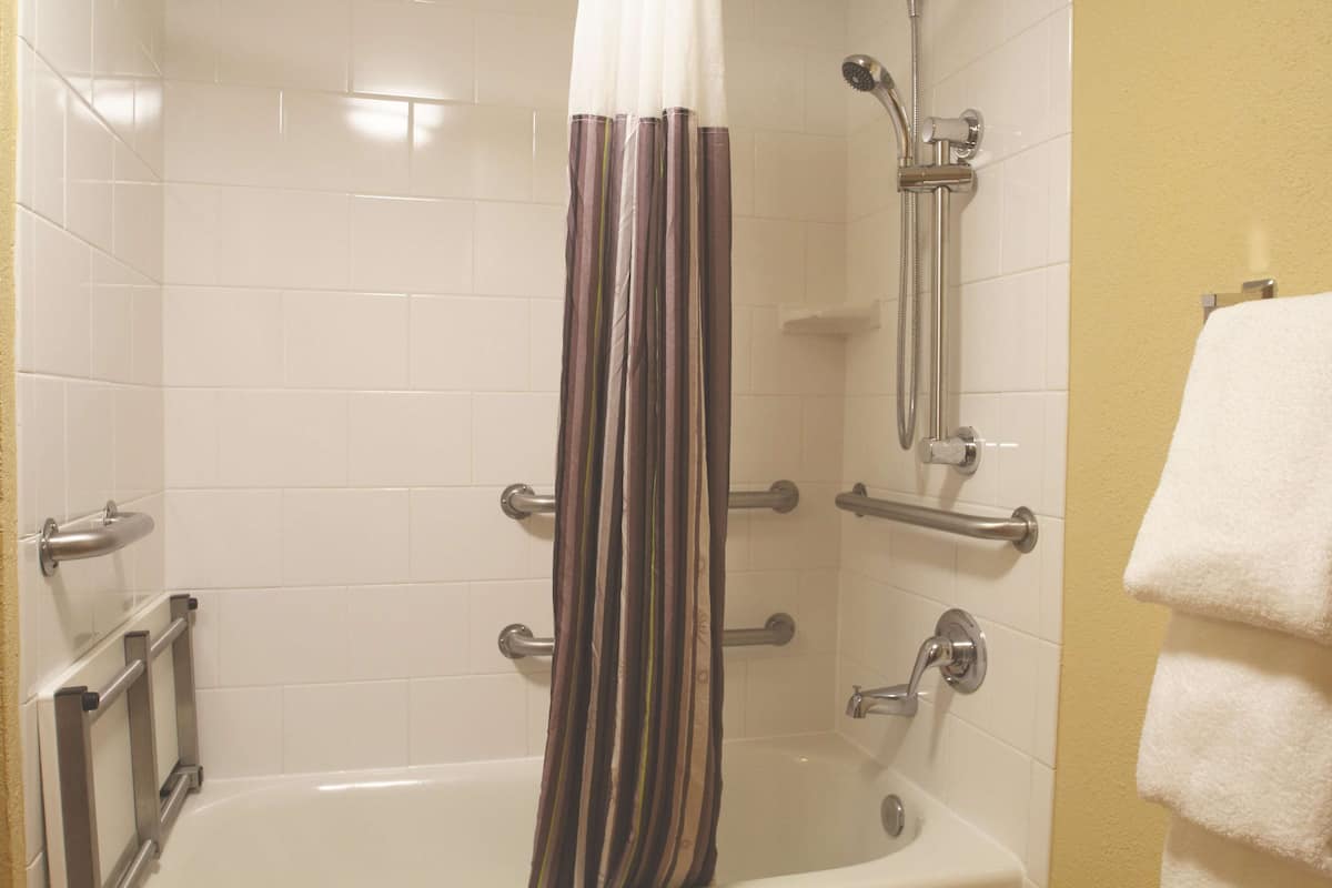 Un baño con ducha, barras de apoyo, una bañera blanca y un perchero para toallas.