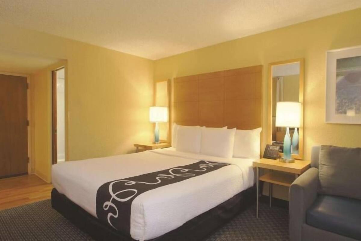 Habitación de hotel con cama, mesita de noche, lámpara y sofá.