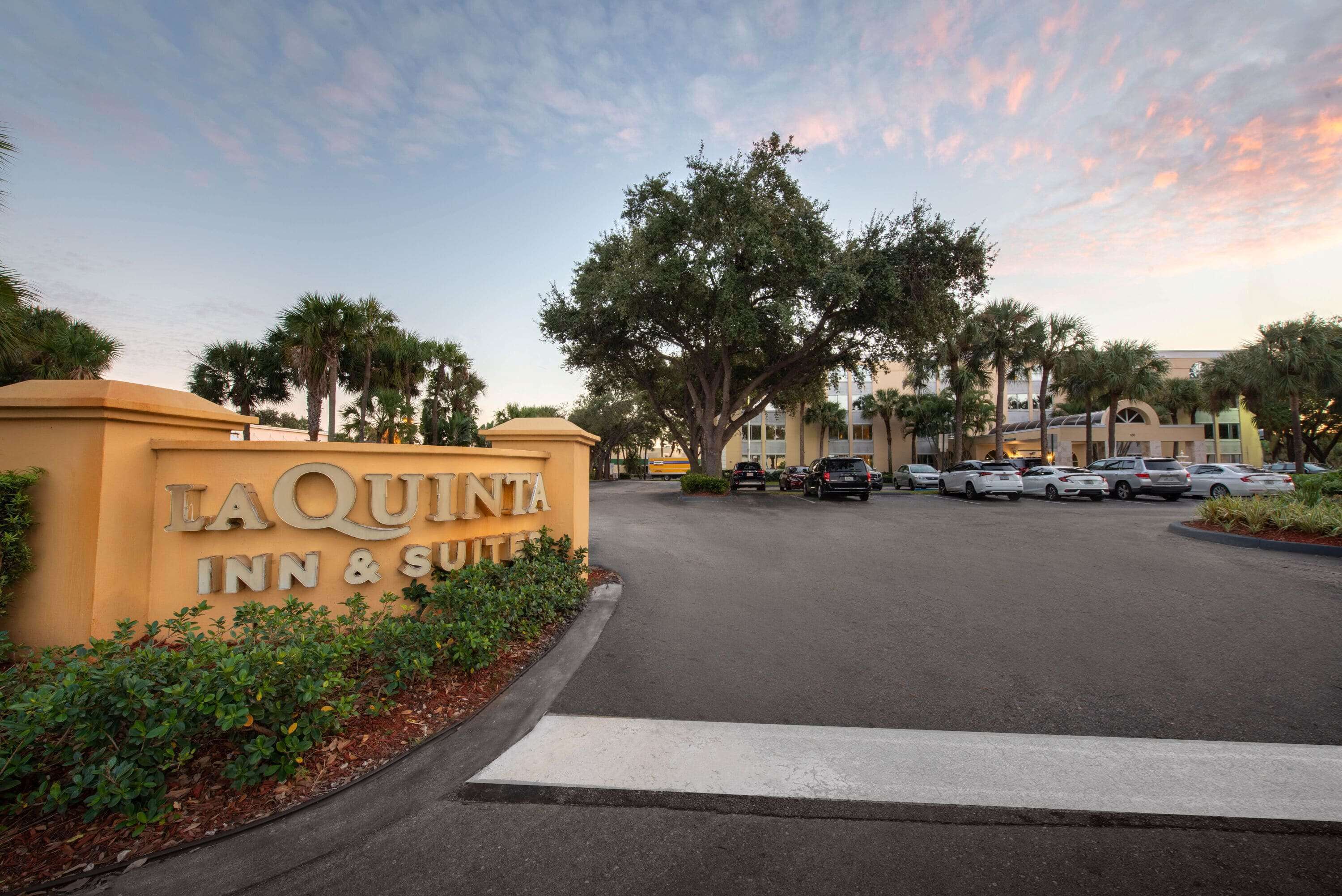 L’entrée d’un hôtel, avec une enseigne indiquant « LAQUINTA INN & SUITES », un parking et des palmiers.