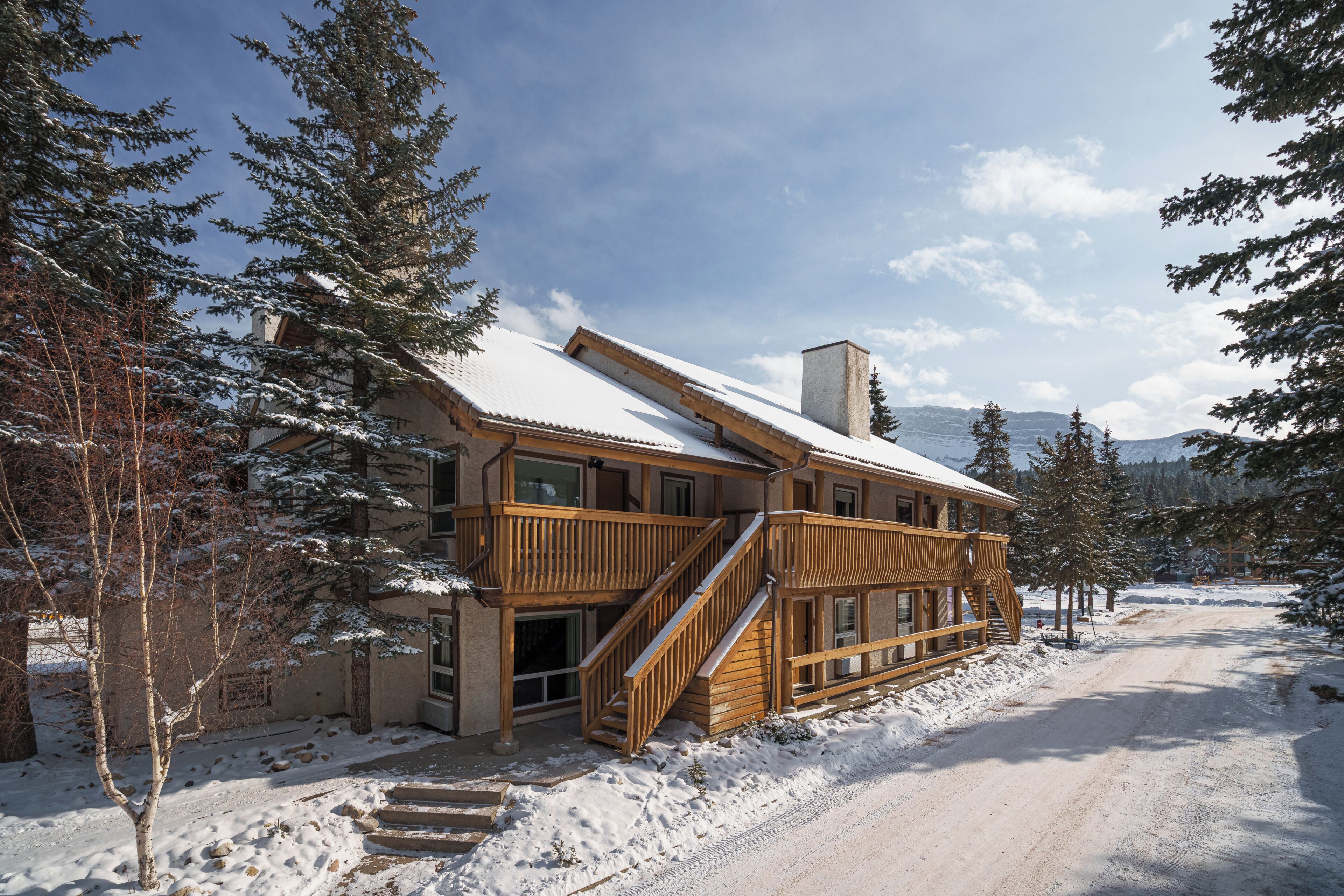 A wooden cabin with a snow-covered roof, surrounded by trees and a clear sky.