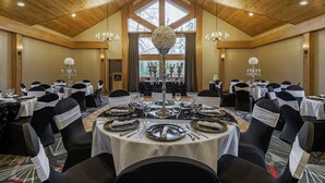 Une salle de banquet avec de hauts plafonds, des lustres et de grandes fenêtres. Les tables sont dressées avec des nappes blanches et des chaises noires.