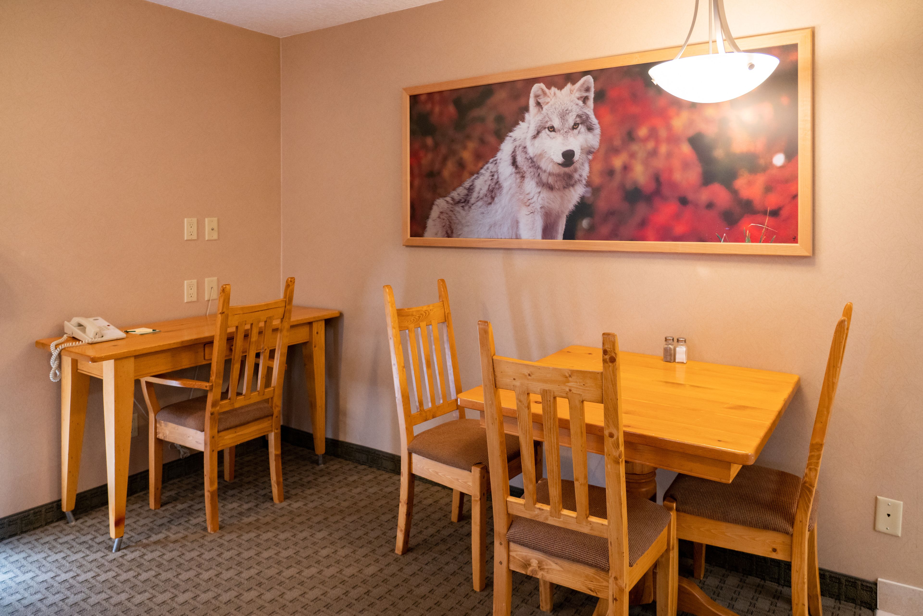 A dining area with a wooden table and chairs, a framed picture of a wolf on the wall, and a hanging light fixture.