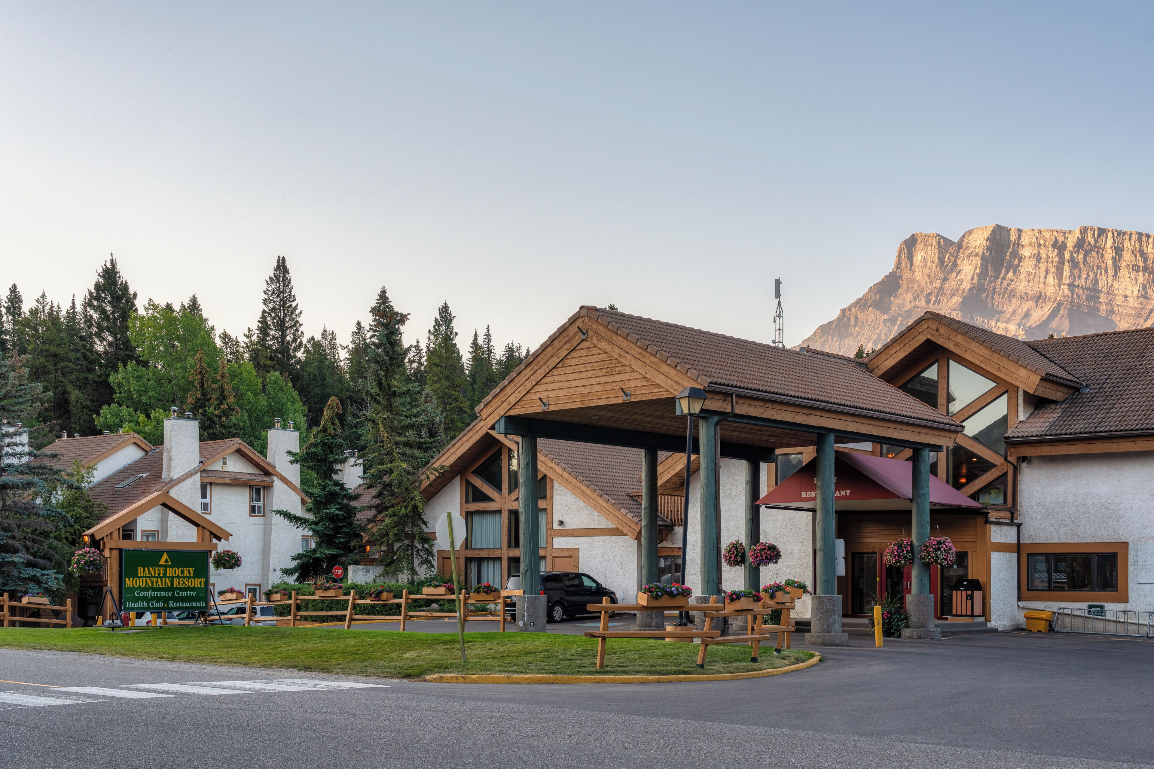 A mountain resort with a covered entrance, wooden buildings, and a mountain backdrop.