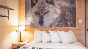A hotel room with a wooden headboard, a large wolf poster, a bedside lamp, a phone, and a bed with a patterned blanket.