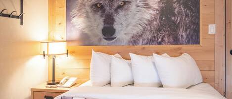 A hotel room with a wooden headboard, a large wolf poster, a bedside lamp, a phone, and a bed with a patterned blanket.