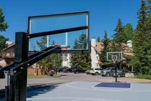 An outdoor basketball court with a clear blue sky, surrounded by residential buildings and parked cars. - Banff Rocky Mountain Resort (Banff)