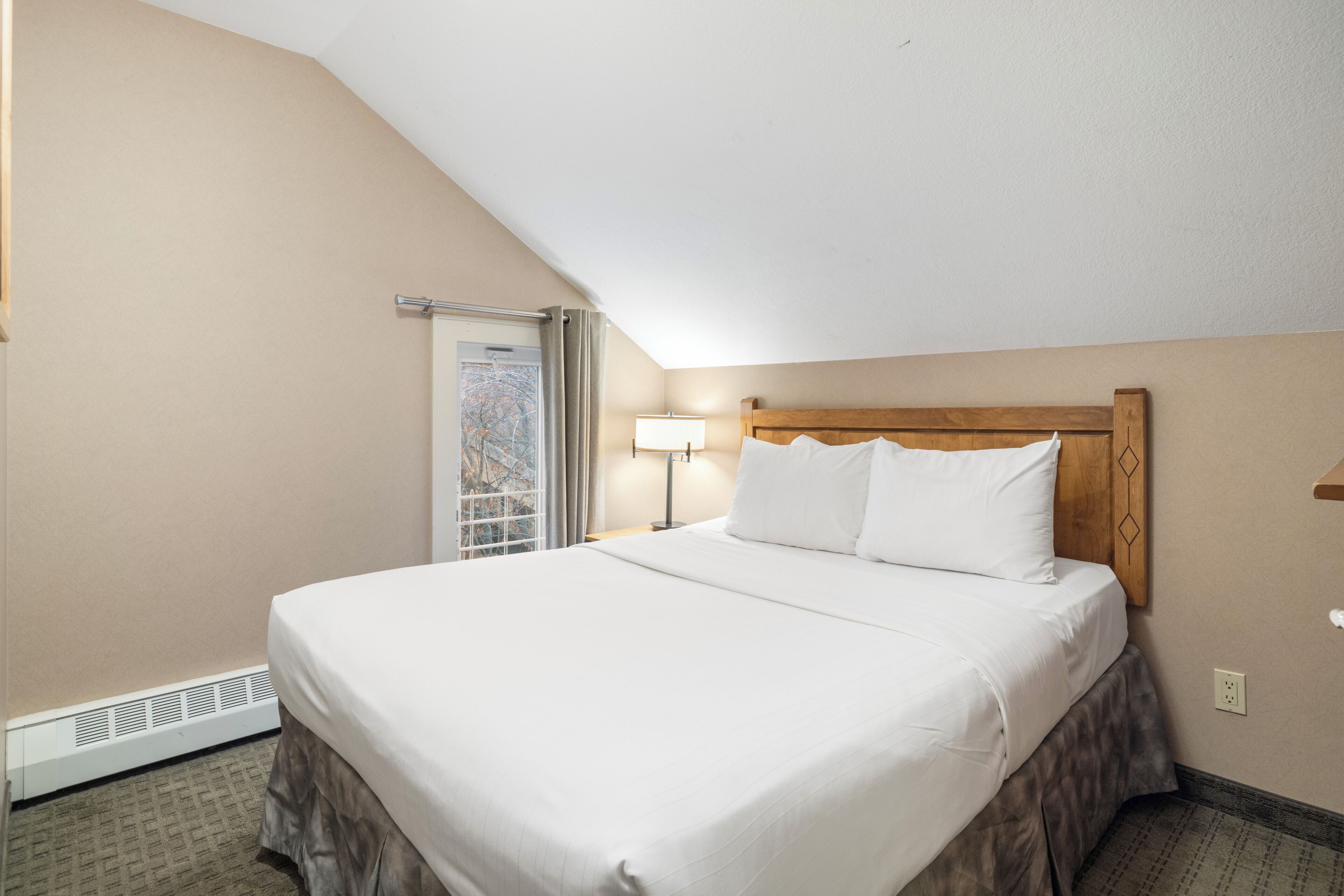 Une chambre d’hôtel avec un lit simple, une fenêtre avec des rideaux, une lampe de chevet et un thermostat.
