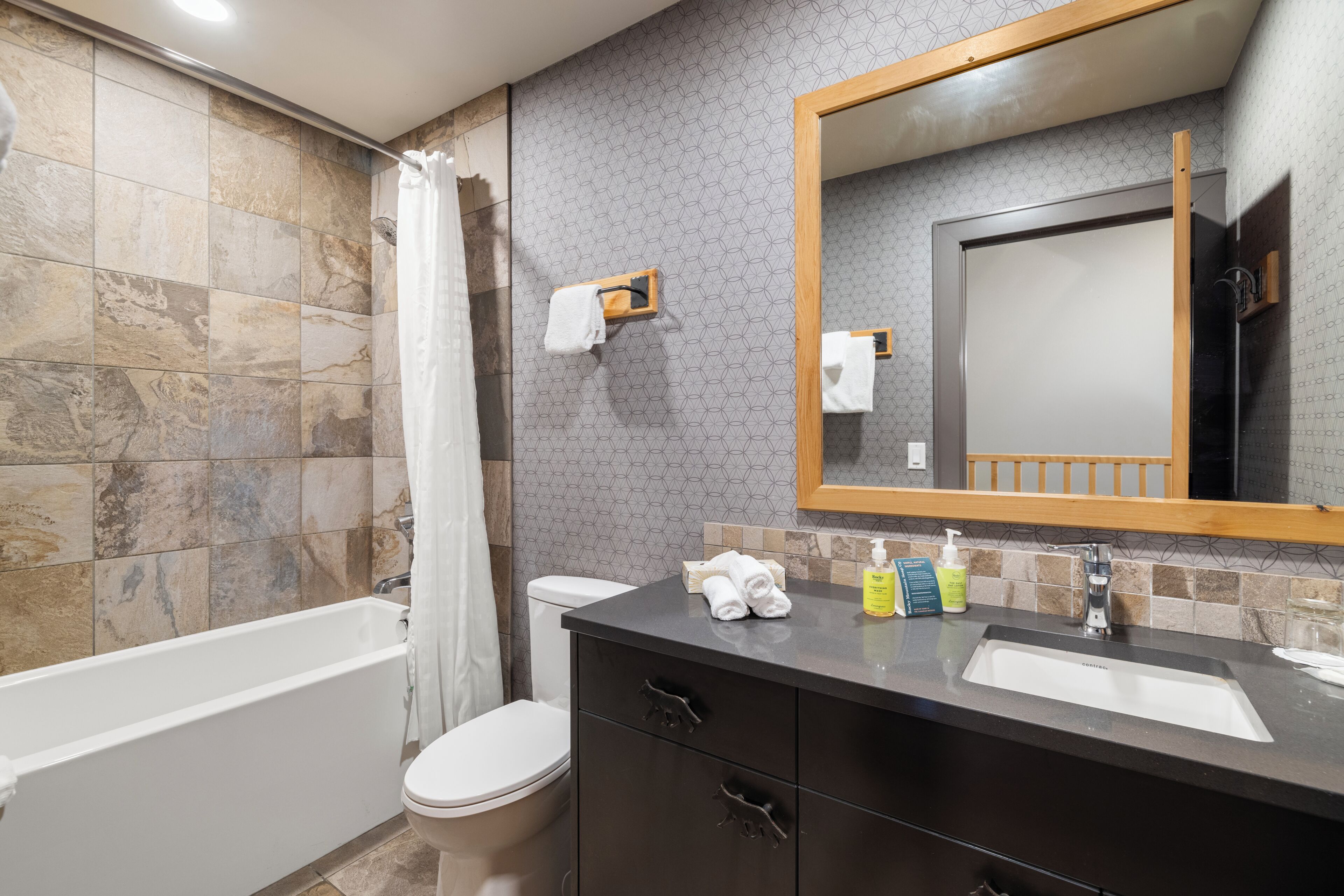 A bathroom with a bathtub, toilet, vanity with a mirror, and toiletries.