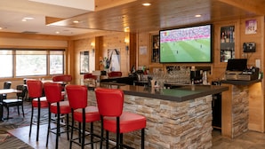 A bar area with a stone counter, red bar stools, and a large TV screen displaying a sports event.