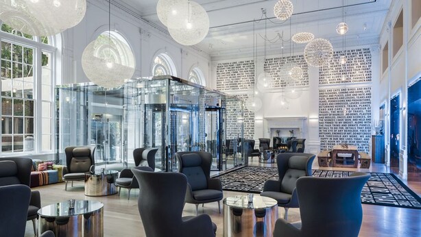 En modern entréhall med glasväggar, svarta sittmöbler och ett stort soffbord i mitten.